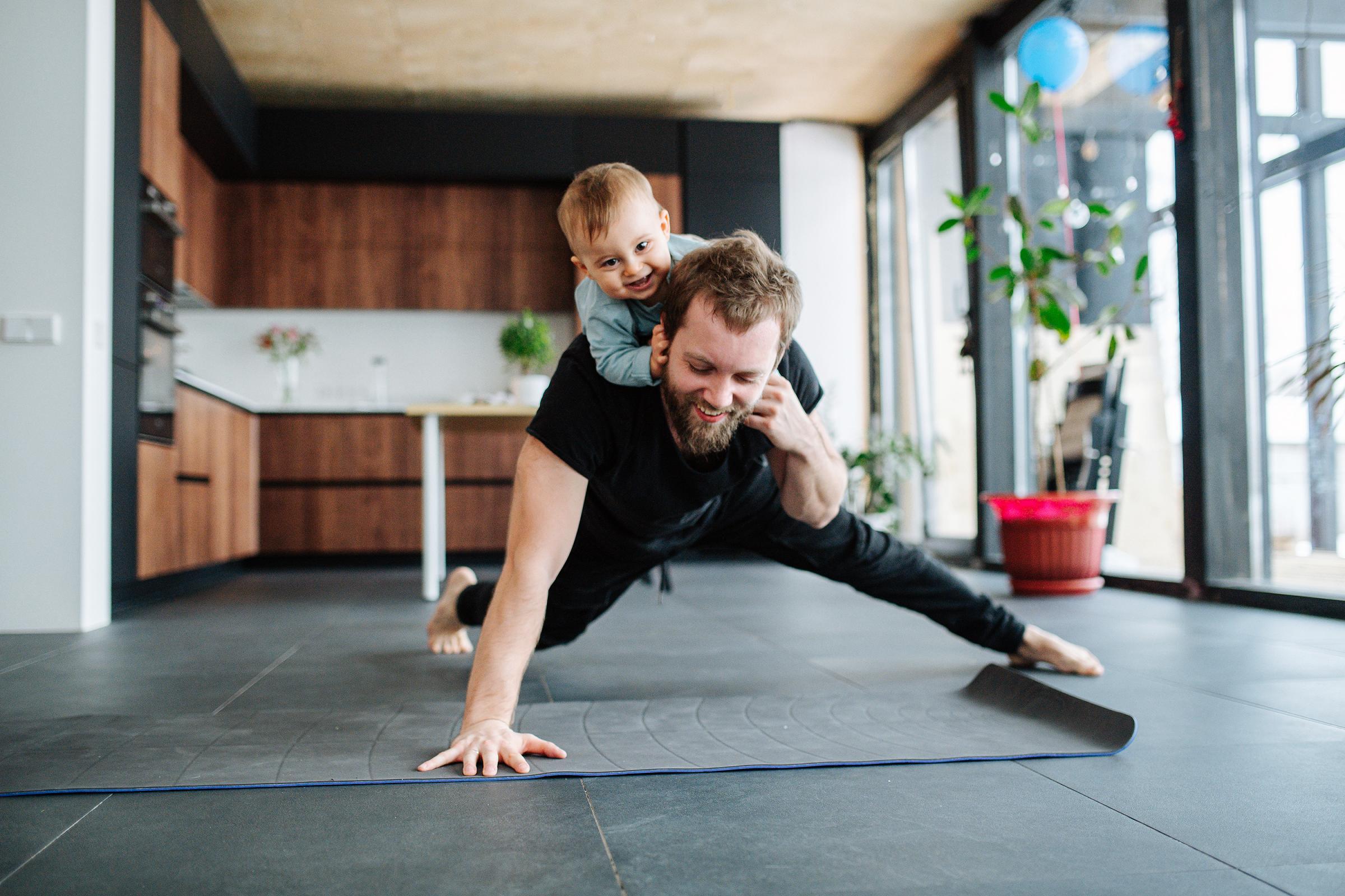 Father working out in living room with small child climbing atop his back 父亲在客厅锻炼,小孩爬在他背上